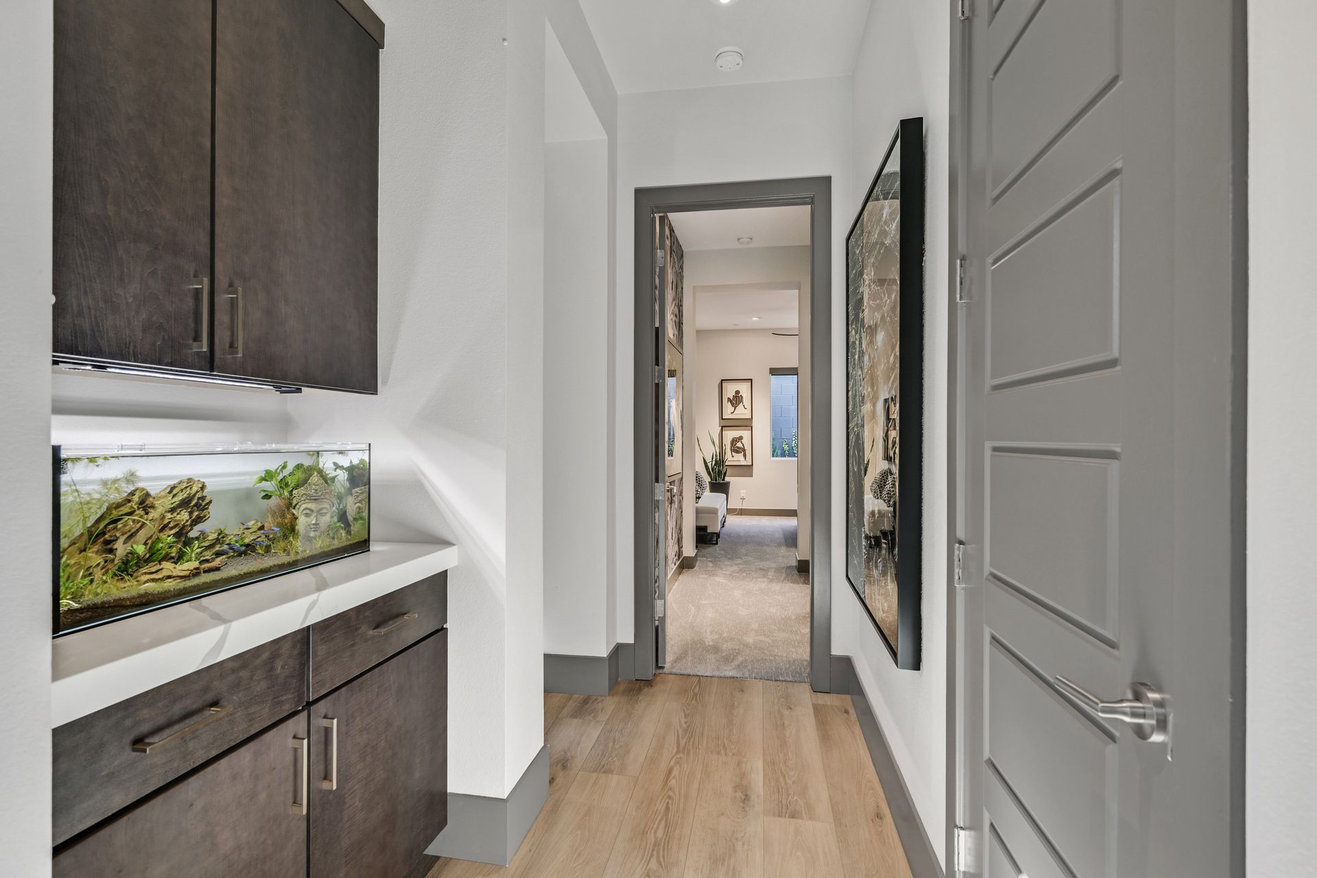 Narrow hallway with aquarium, dark cabinets, and artwork. Light wood flooring and grey trim.