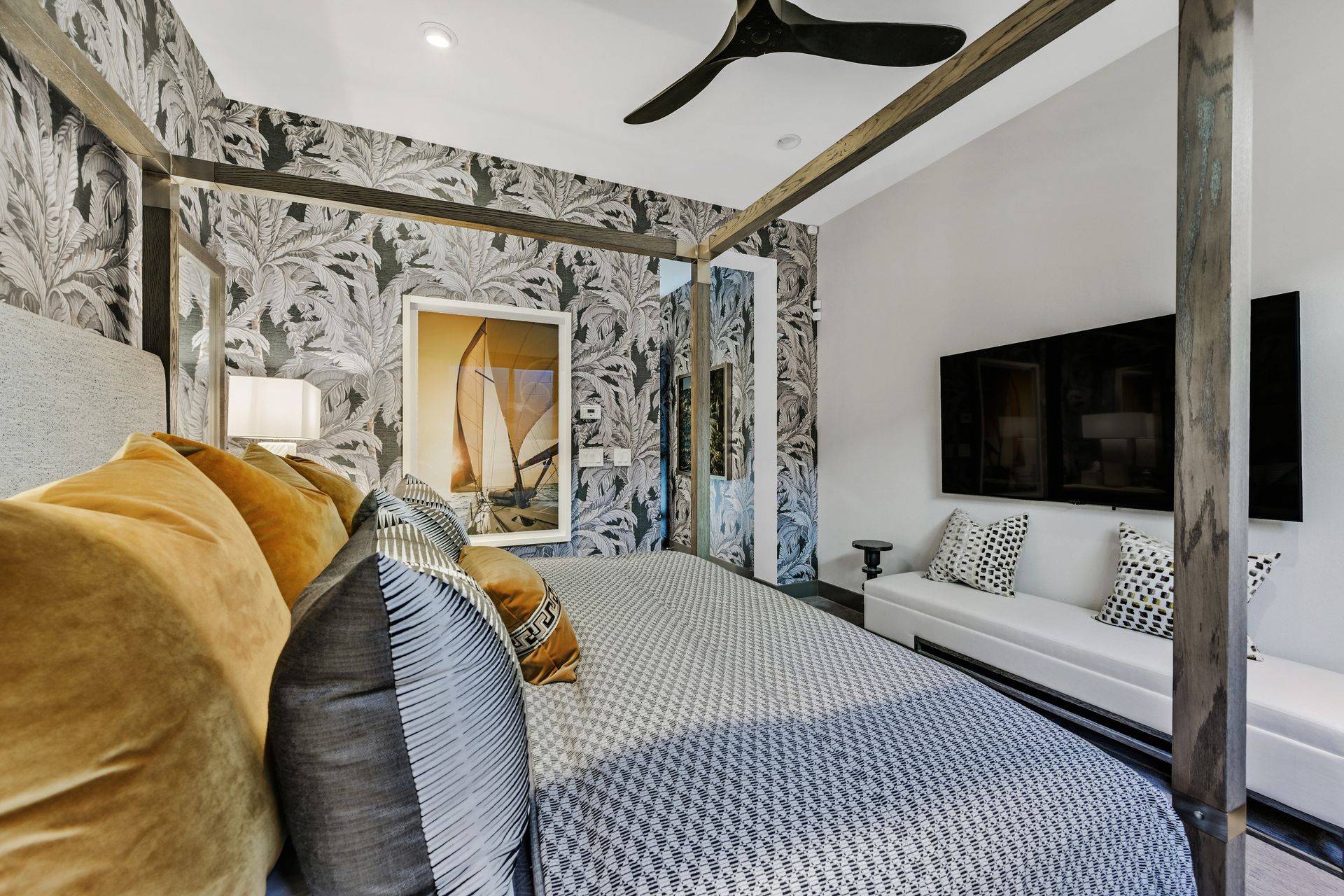 Bedroom with canopy bed, patterned wallpaper, gold pillows, and a wall-mounted TV.