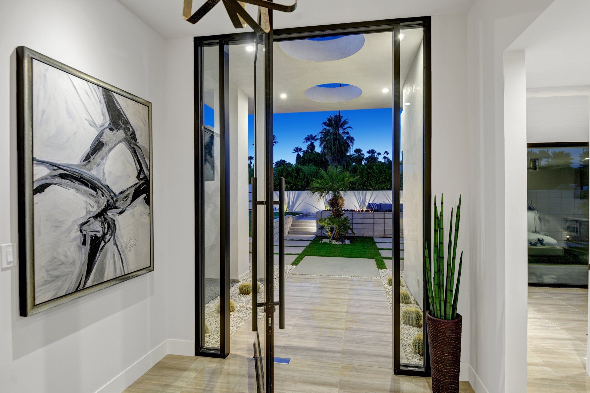 Entryway with open glass doors, artwork, white walls, and a glimpse of an outdoor garden.