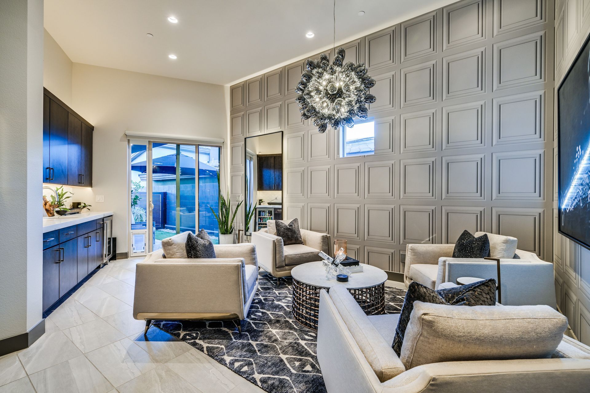 Living room with gray paneled wall, modern furniture, and a large chandelier.