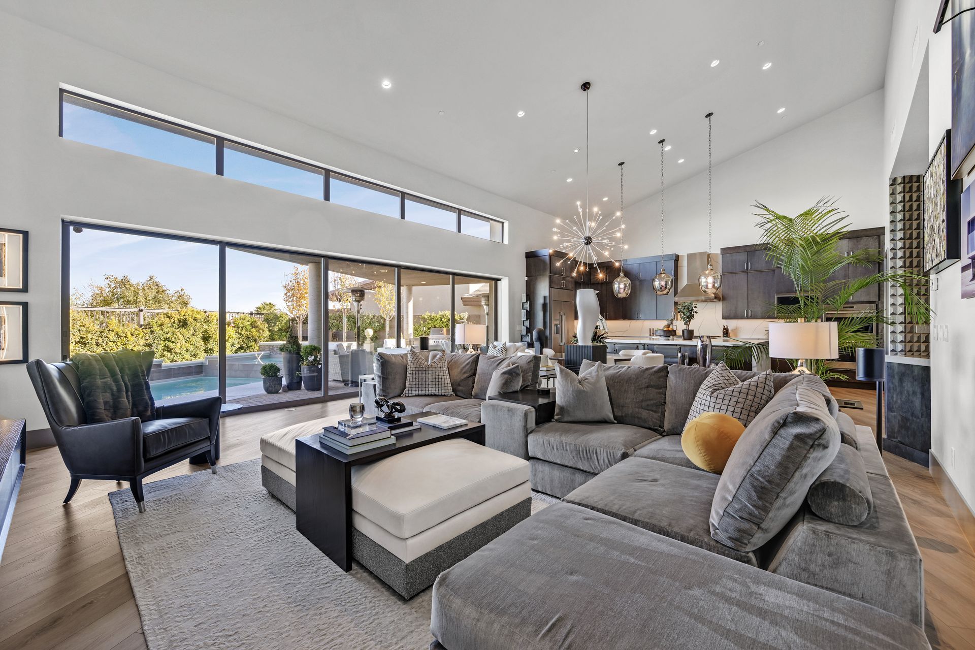 Spacious living room with large gray sectional, open to kitchen and outdoor patio with pool.