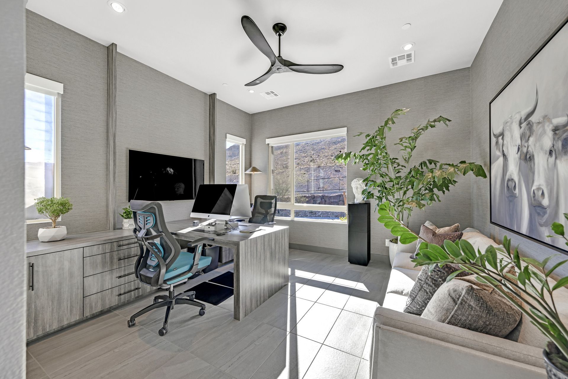 Modern home office with desk, computer, sofa, and a large artwork of cows.