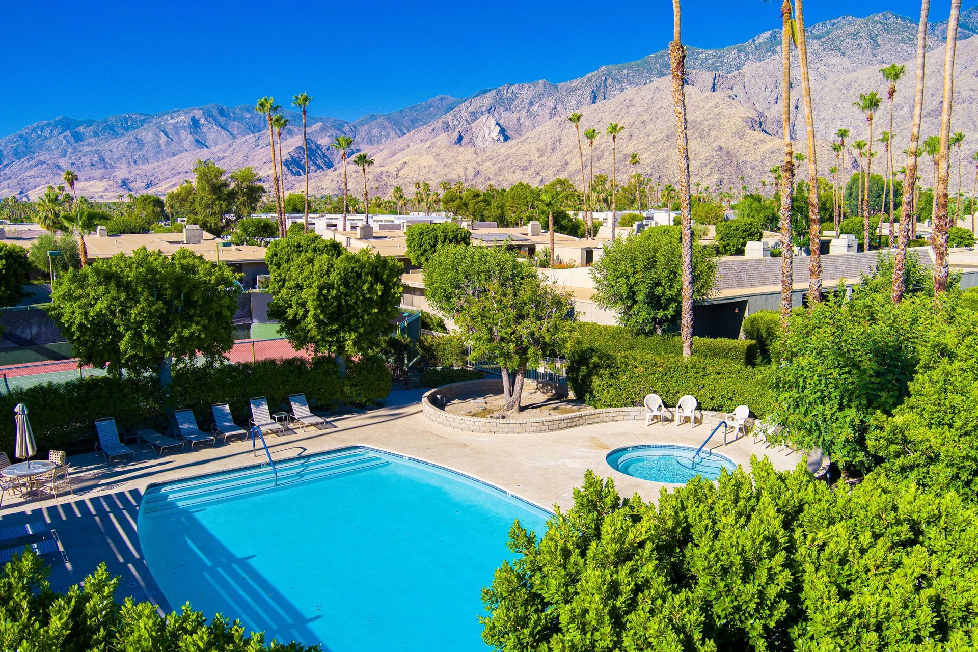 An aerial view of a large swimming pool surrounded by palm trees and mountains.