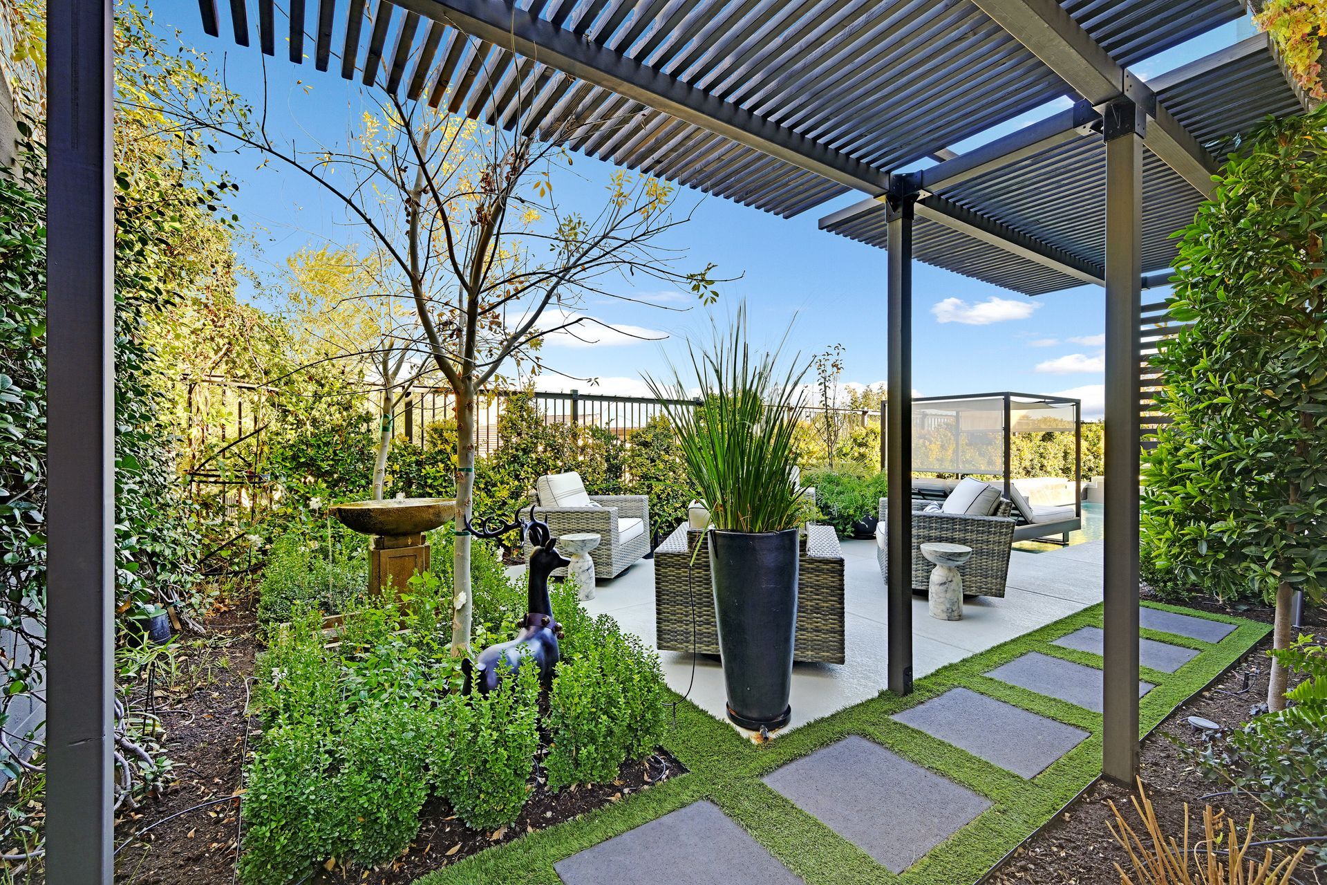 Outdoor patio with seating around a fire pit, water feature, and lush greenery.