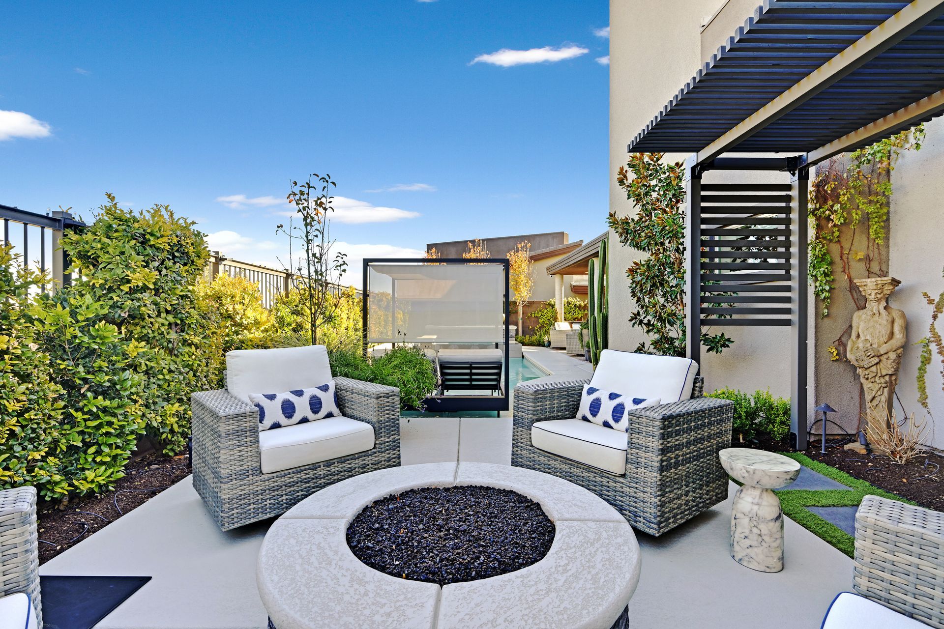 Patio with fire pit, seating, and partially shaded lounging area; sunny day, blue sky.