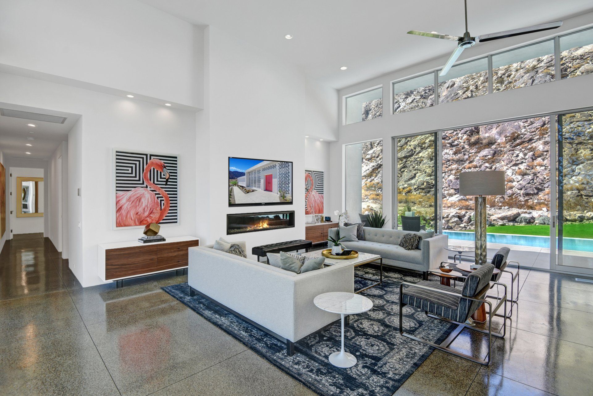 Modern living room with pool view, white walls, artwork, and a gray couch.