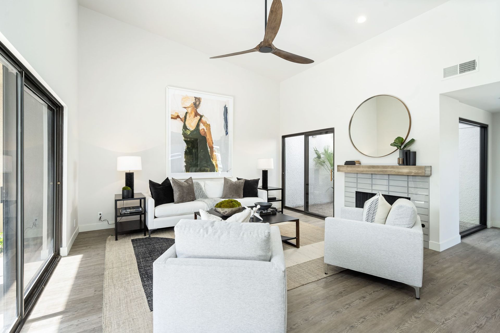 A living room with white furniture , a fireplace , and a ceiling fan.