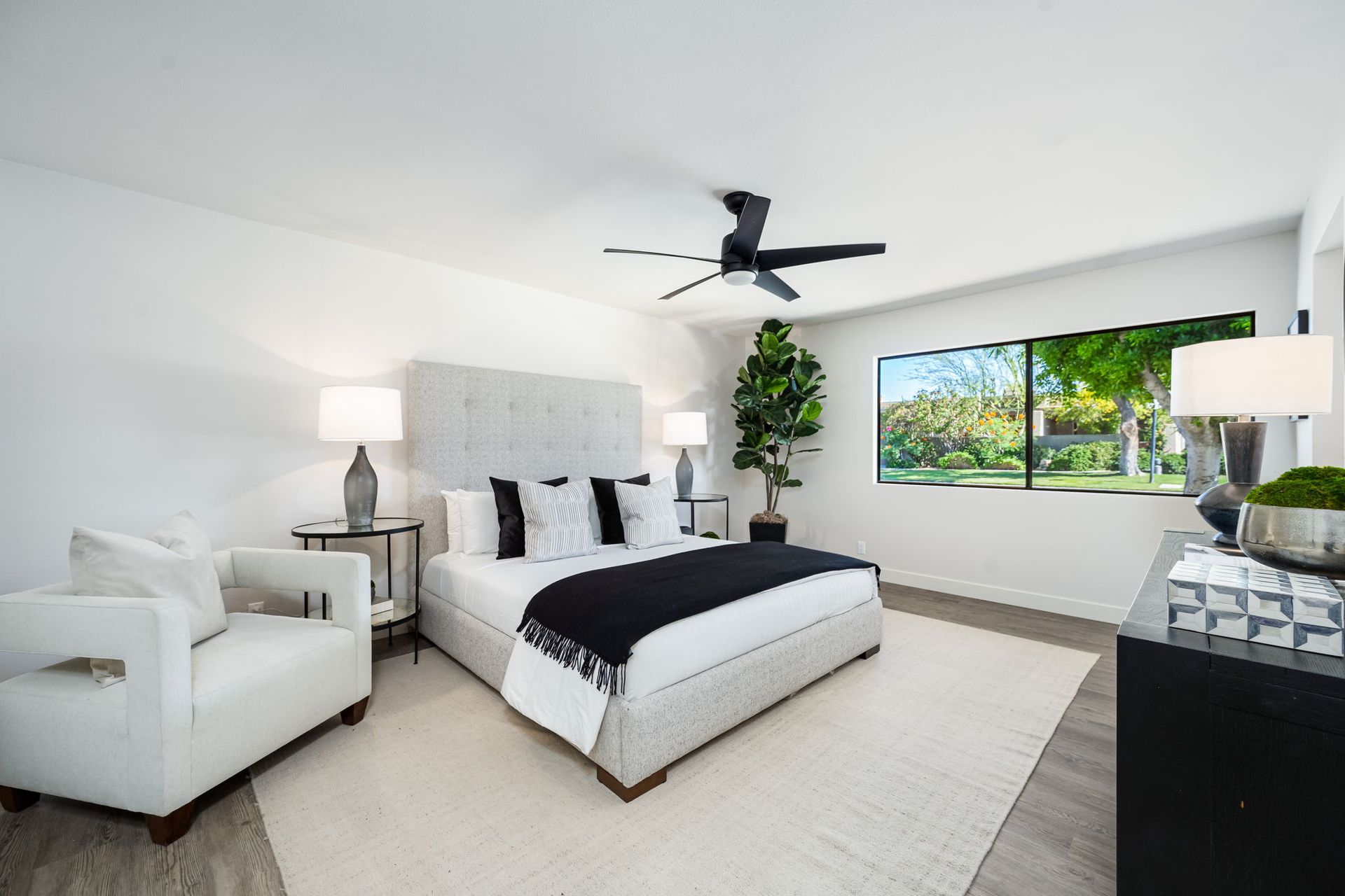 A bedroom with a bed , chair , dresser and ceiling fan.
