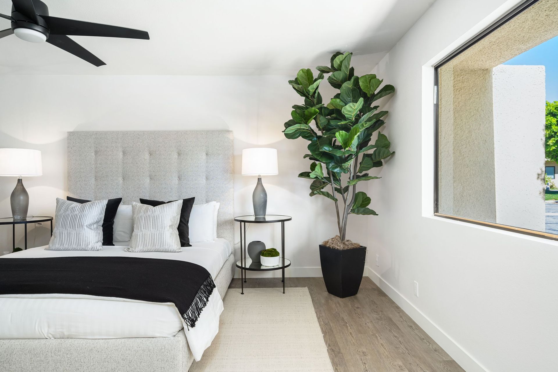 A bedroom with a bed , ceiling fan , nightstands , and a window.