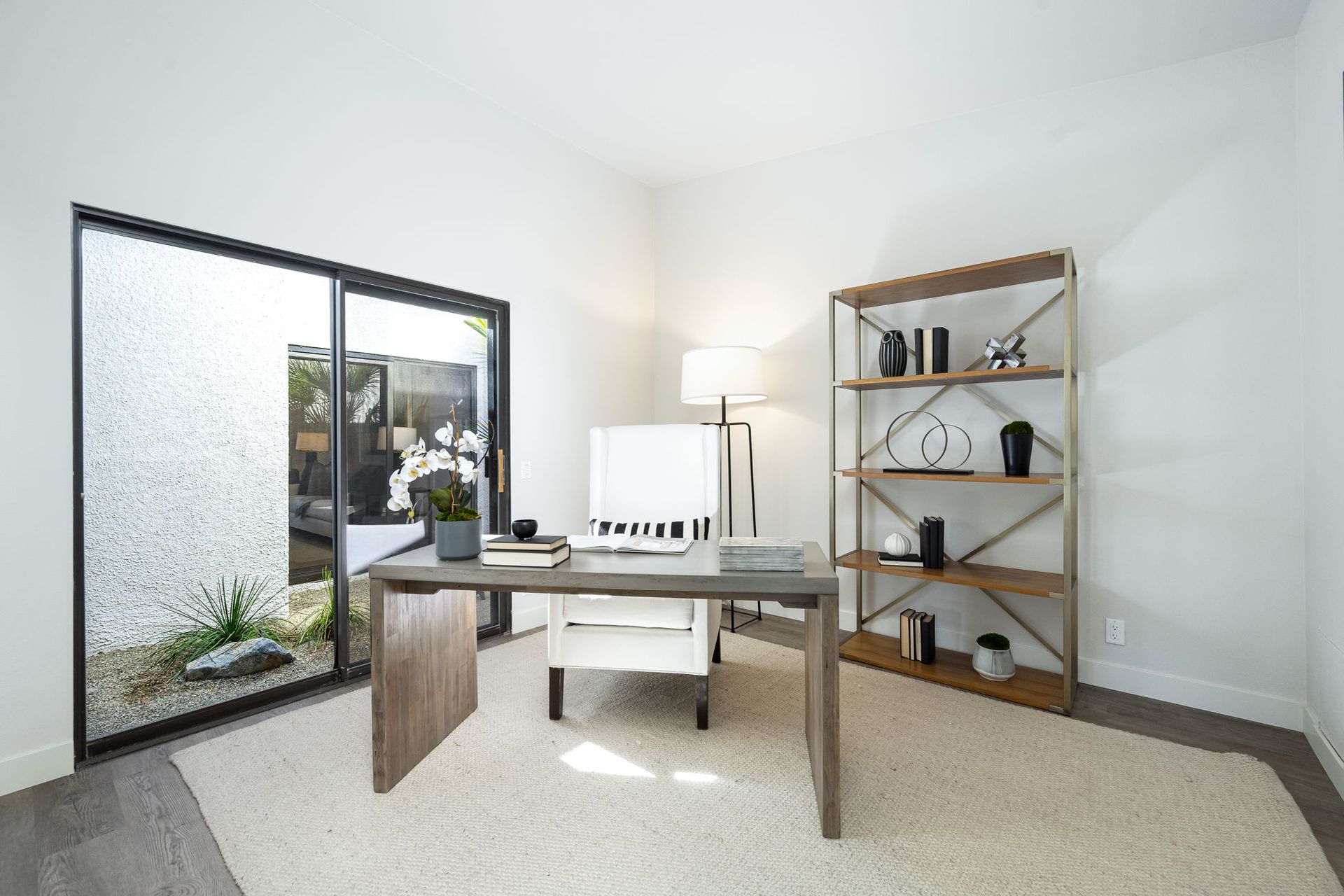 A home office with a desk , chair , bookshelf and sliding glass doors.