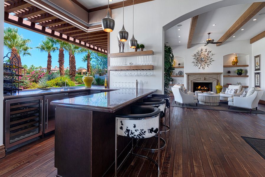 Indoor bar with counter seating, overlooking a backyard oasis with palm trees and a pool.