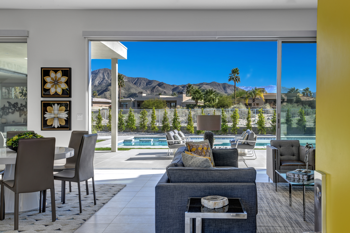 Living room with open view to pool, palm trees, and mountains under a blue sky.