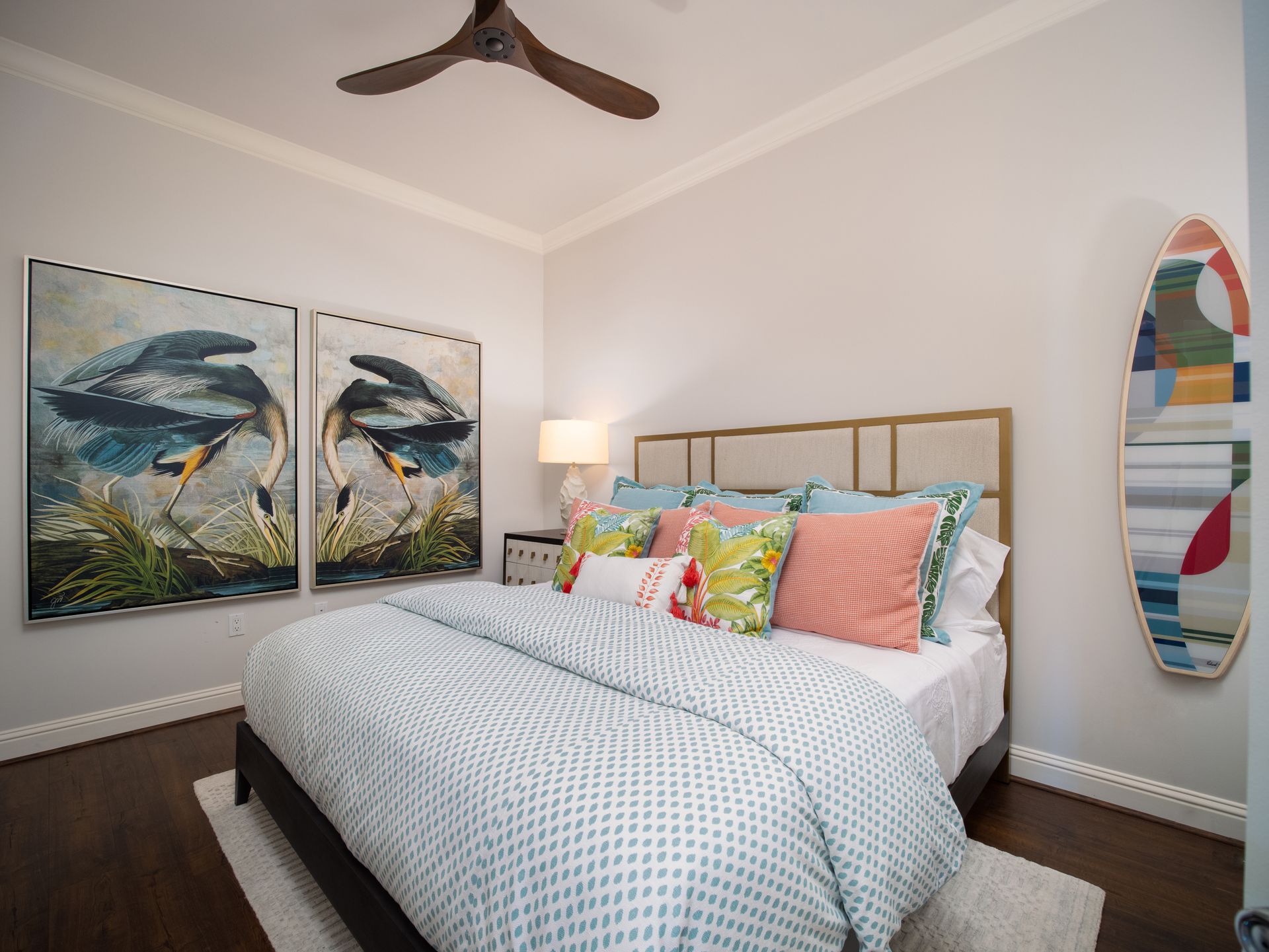 A bedroom with a bed , two paintings on the wall and a ceiling fan.