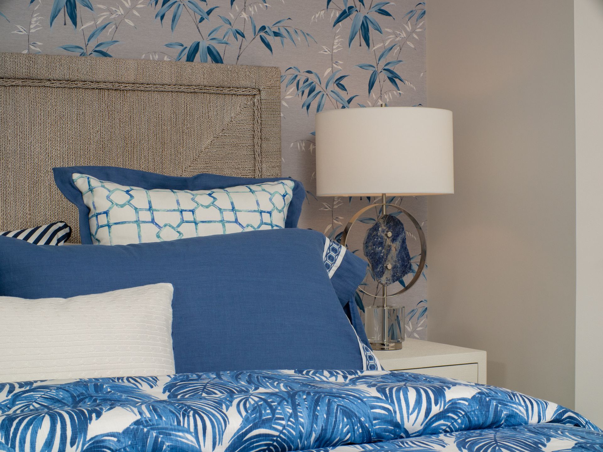 A bed with a blue comforter and white pillows next to a lamp.