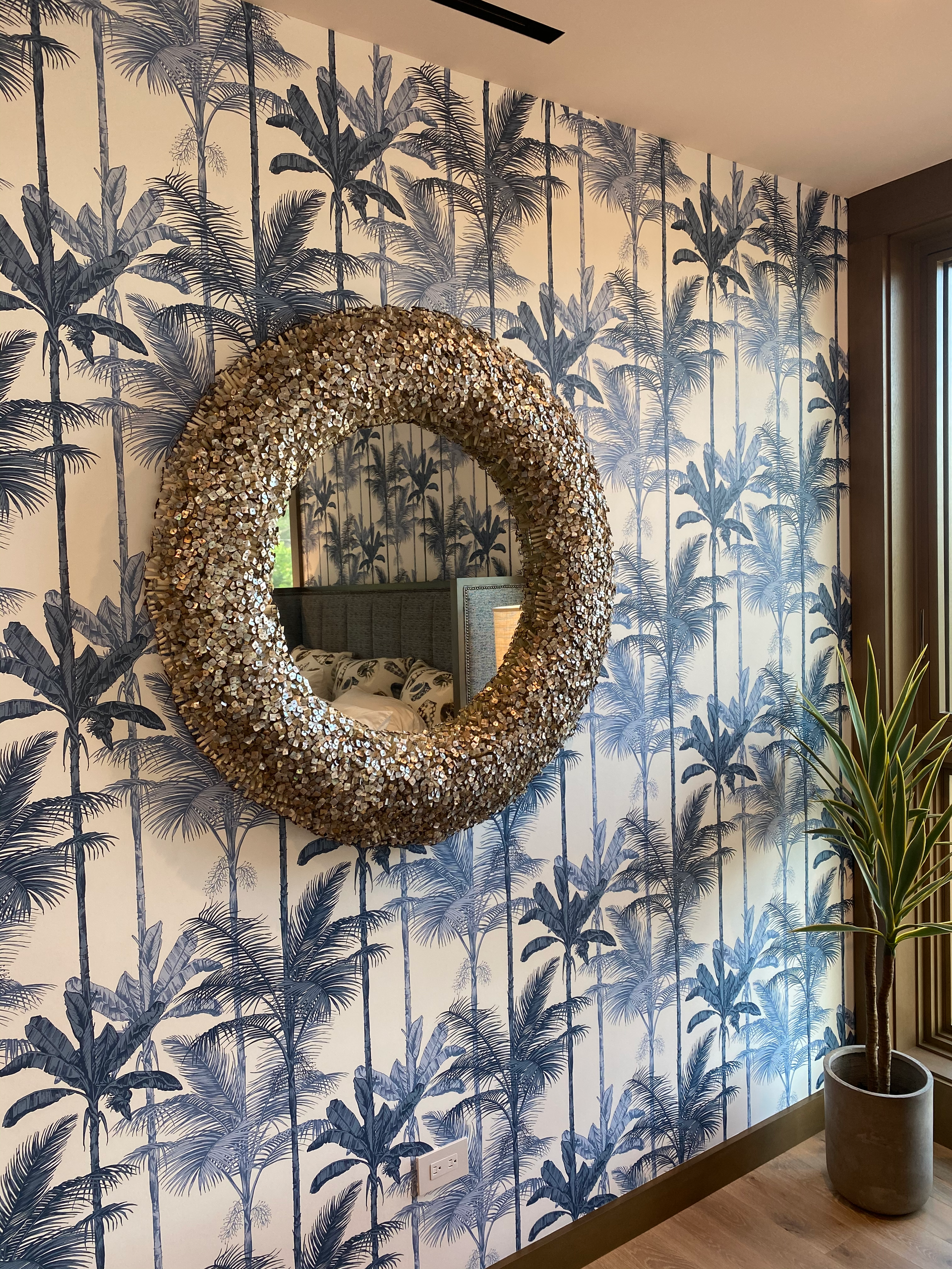 Blue palm tree wallpaper with a round mirror and a potted plant.