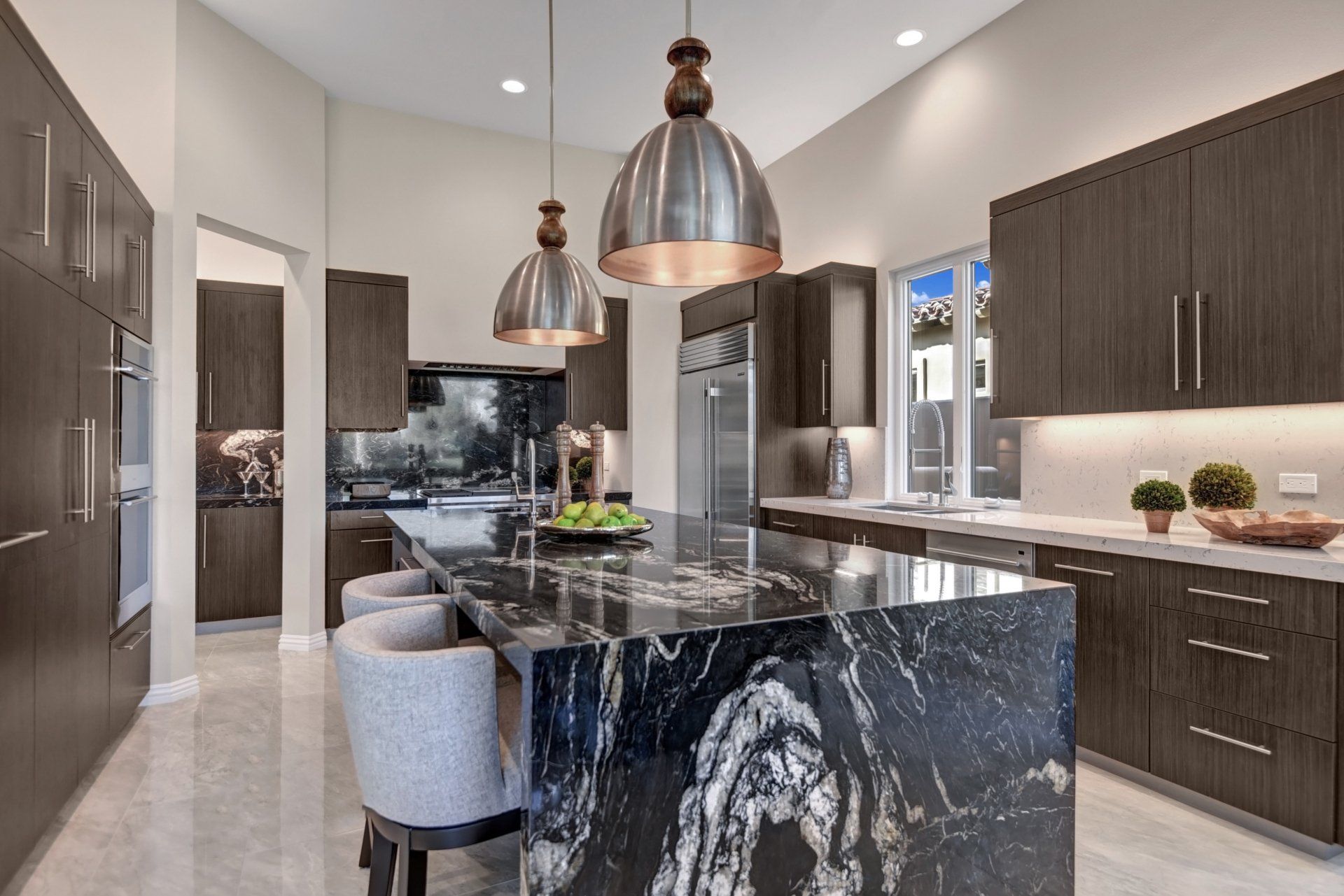 Modern kitchen with dark wood cabinets, a black marble island, and pendant lights.