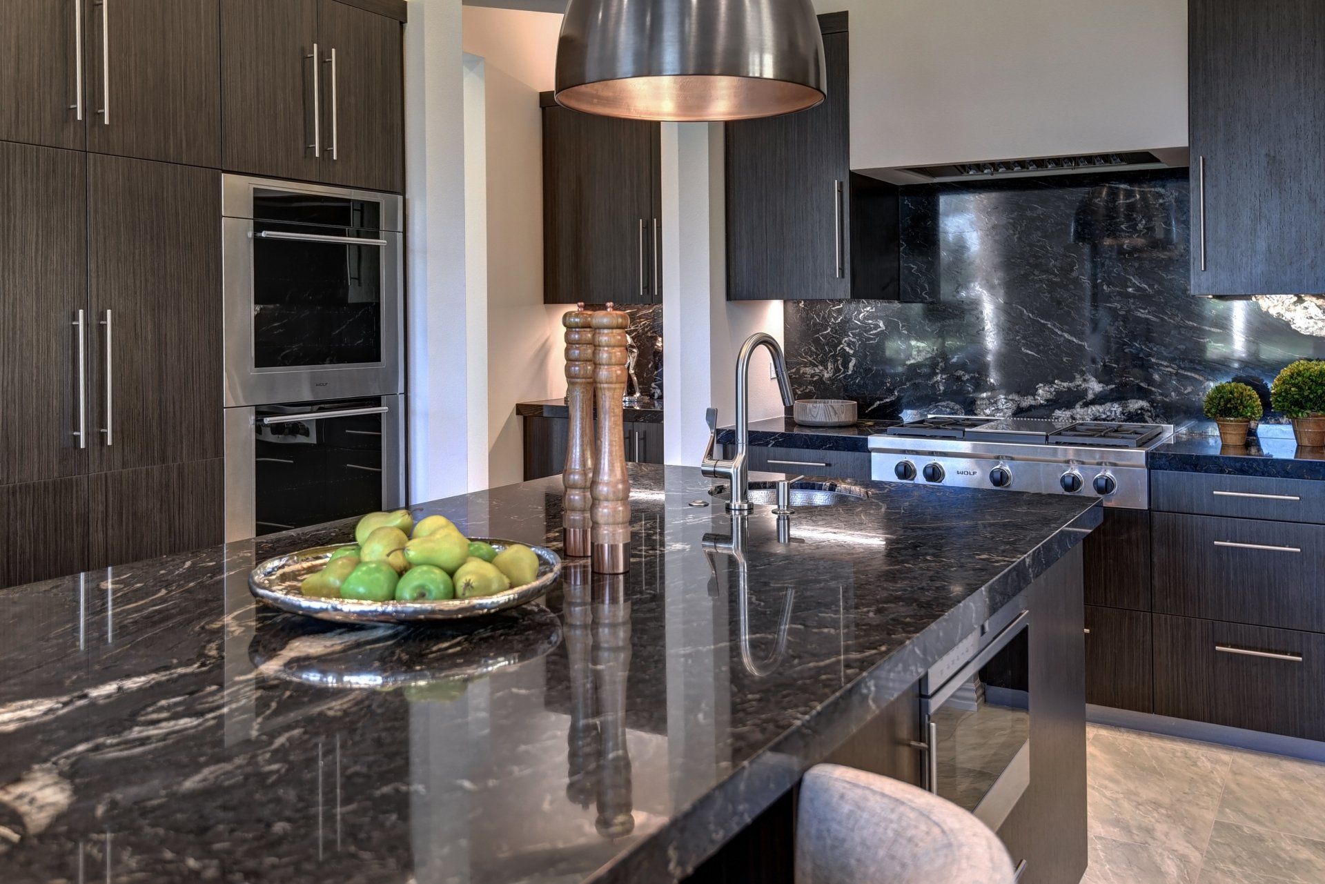 Modern kitchen with dark wood cabinets, black granite countertops, and a fruit bowl.