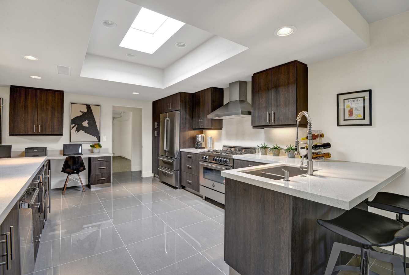 A kitchen with stainless steel appliances , wooden cabinets , a sink , and a skylight.