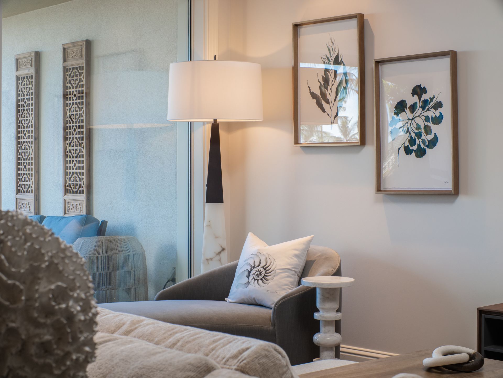 A living room with a couch , chair , lamp and paintings on the wall.