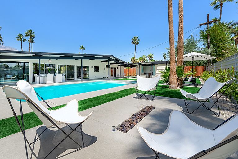 Poolside patio with white butterfly chairs, pool, and modern house.
