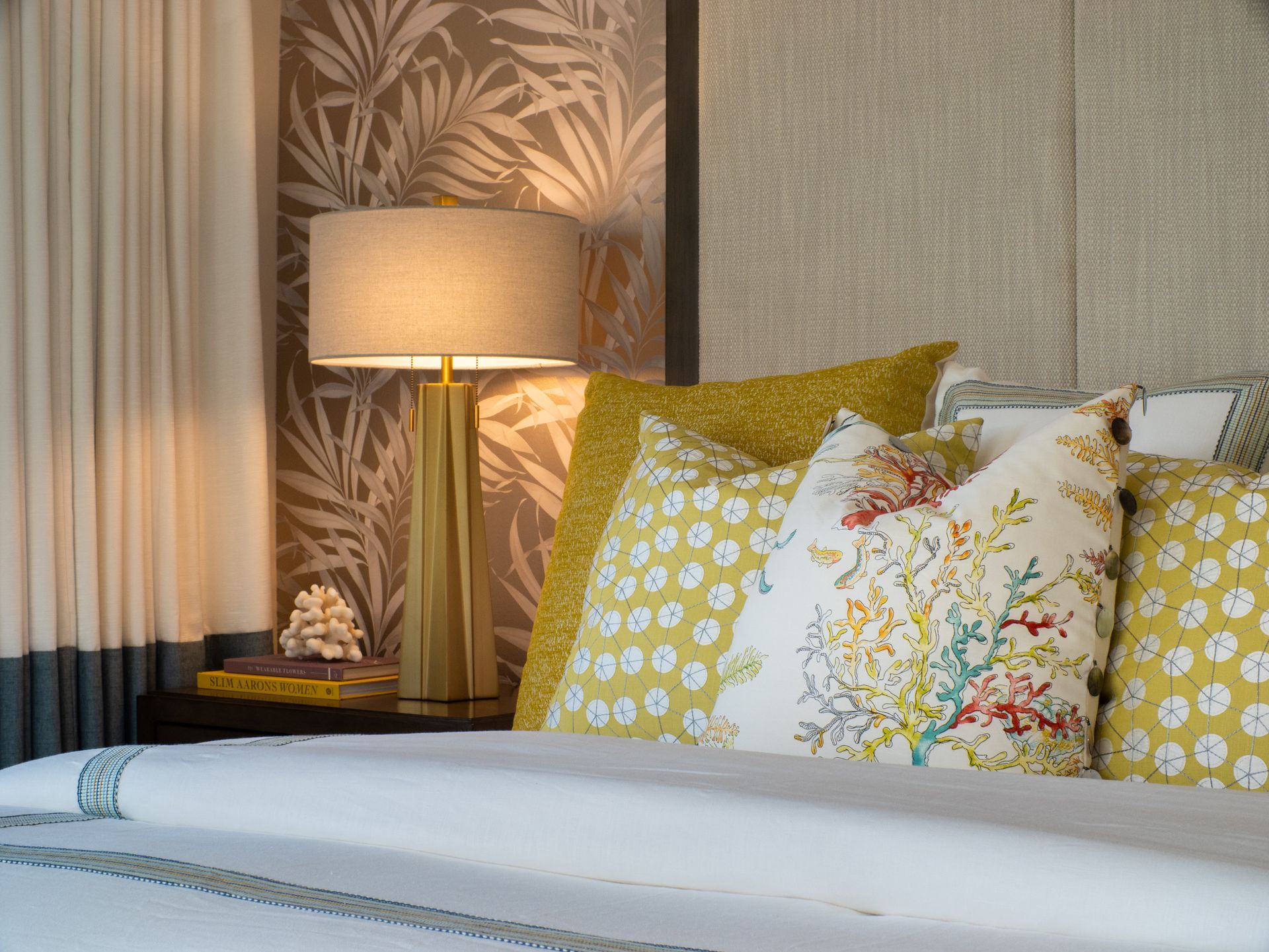 A bedroom with a bed , nightstand , lamp and pillows.