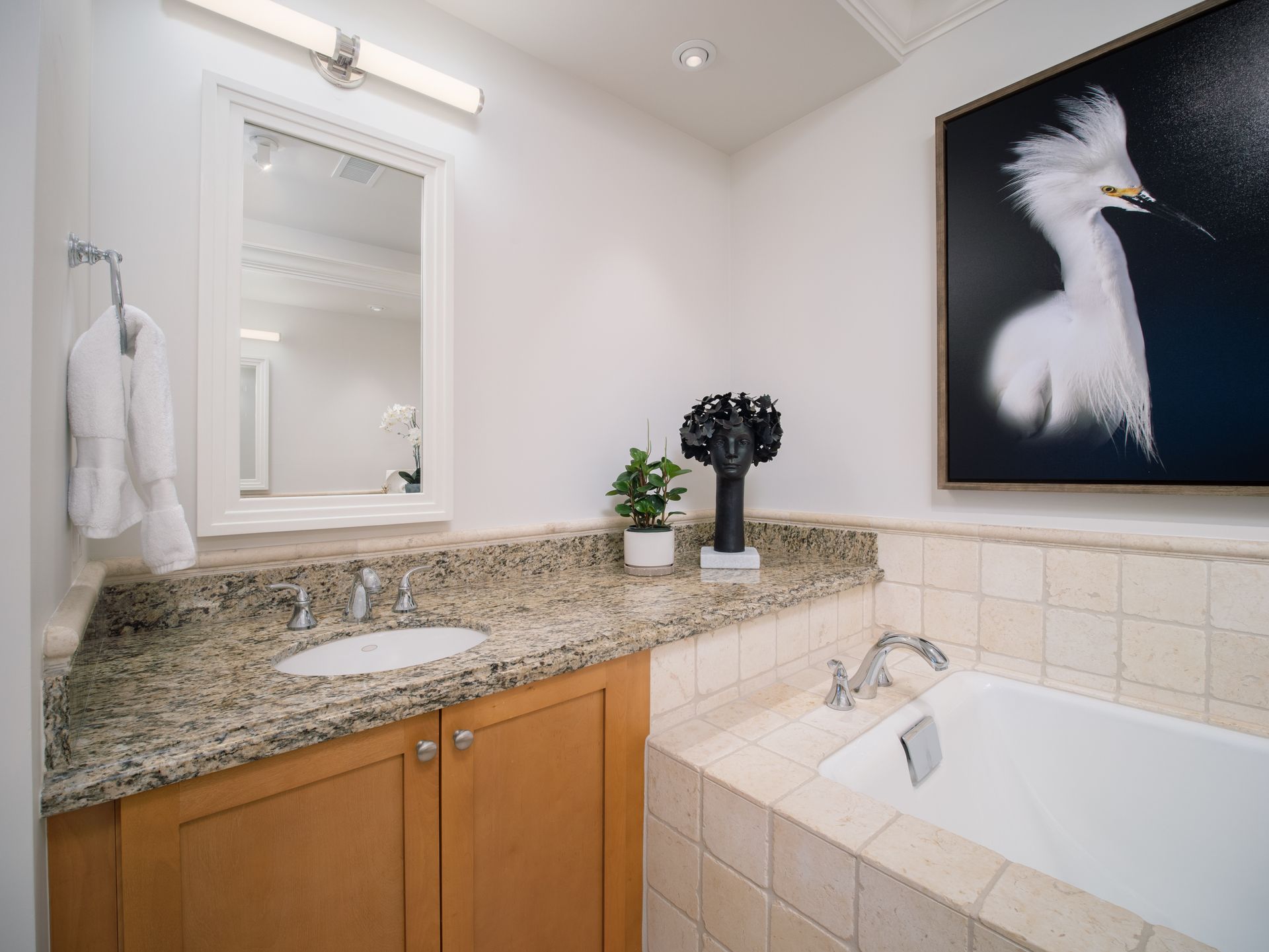 A bathroom with a sink , tub , mirror and a picture of a bird on the wall.