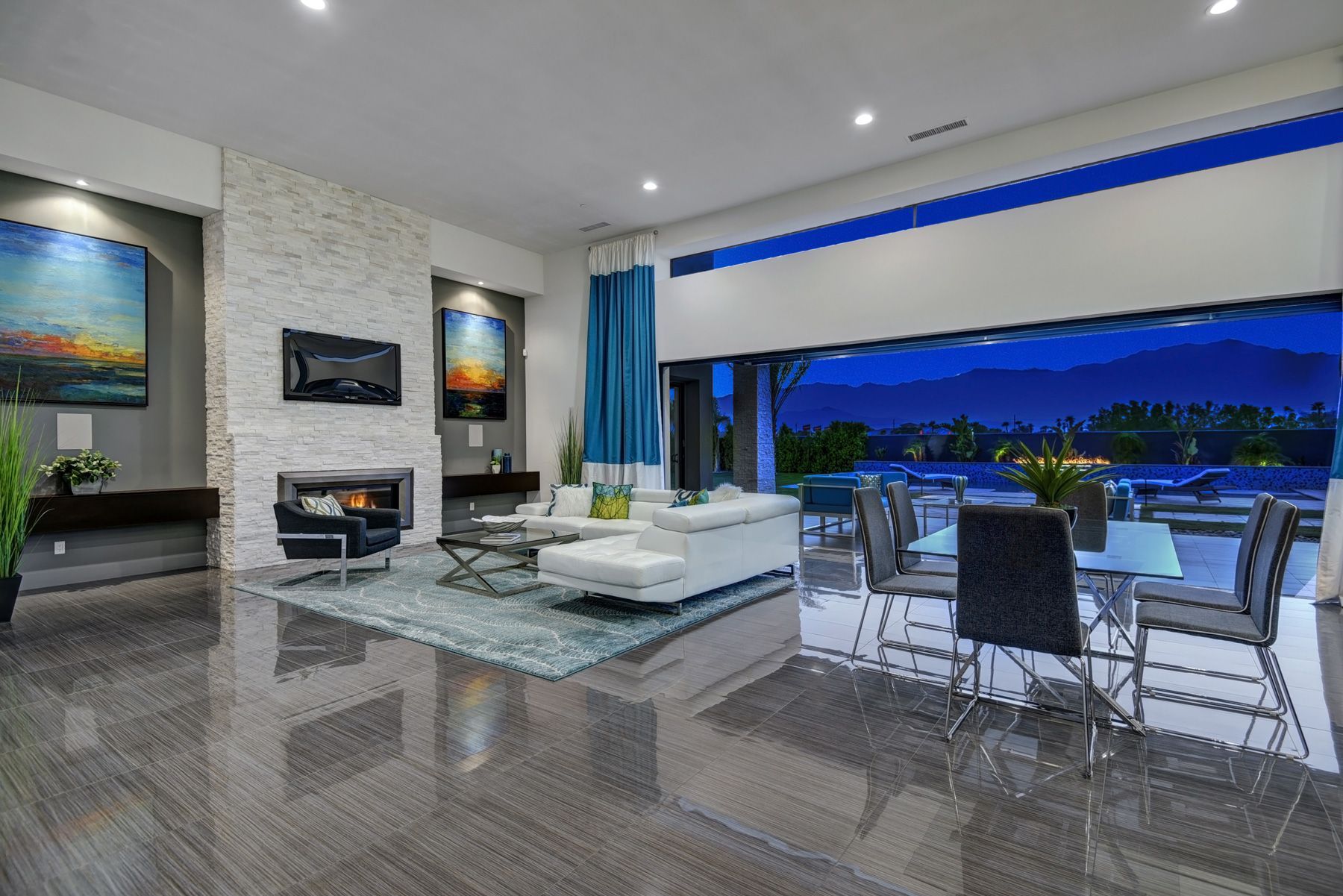 Modern living room with open doors to a nighttime view. White furniture, fireplace, artwork, and a dining table.