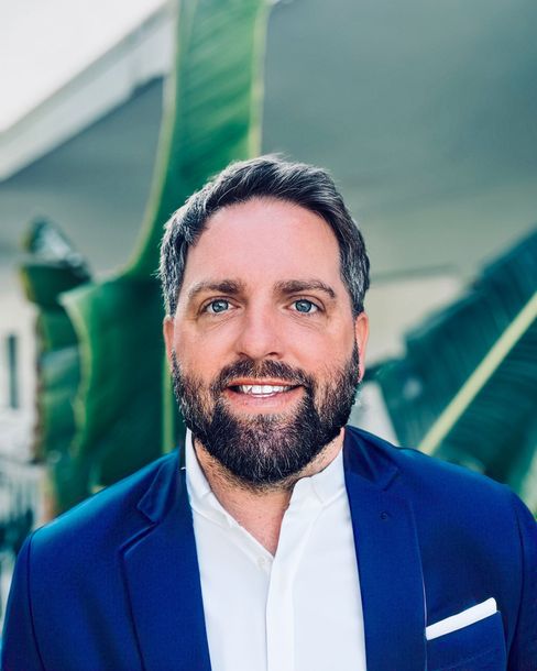 A man with a beard is wearing a blue suit and white shirt.