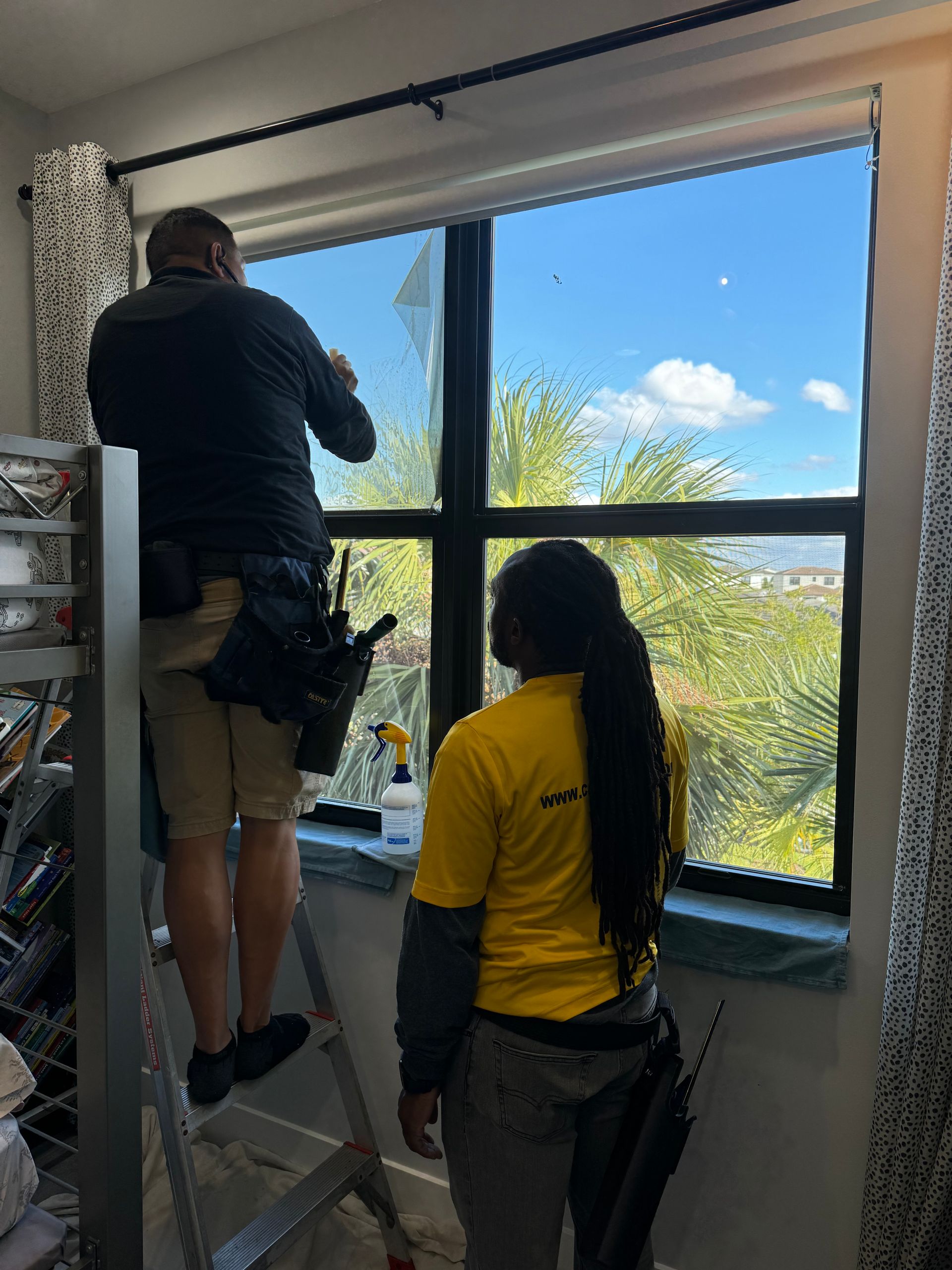 A man and a woman are cleaning a window in a room.
