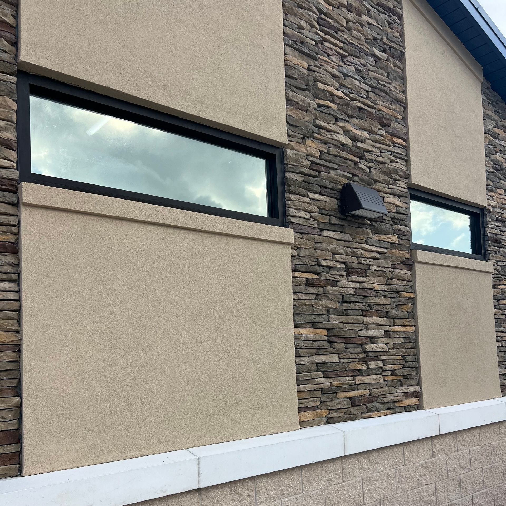 Two windows on the side of a building with a stone wall