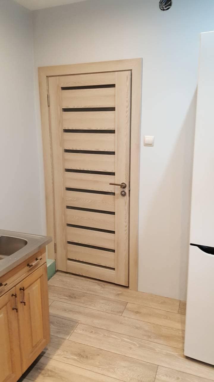 Virtuvė su medinėmis durimis ir baltu šaldytuvu.