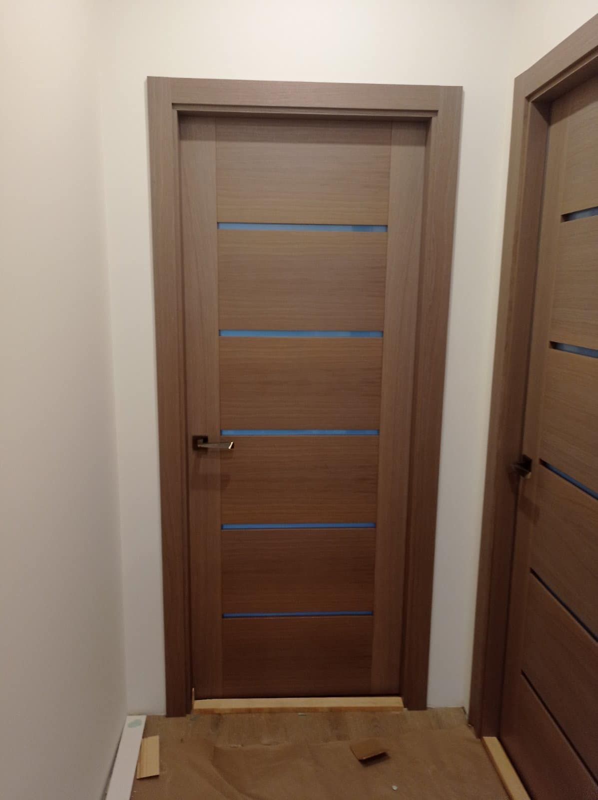 Medinės durys su mėlynomis juostelėmis yra koridoriuje.