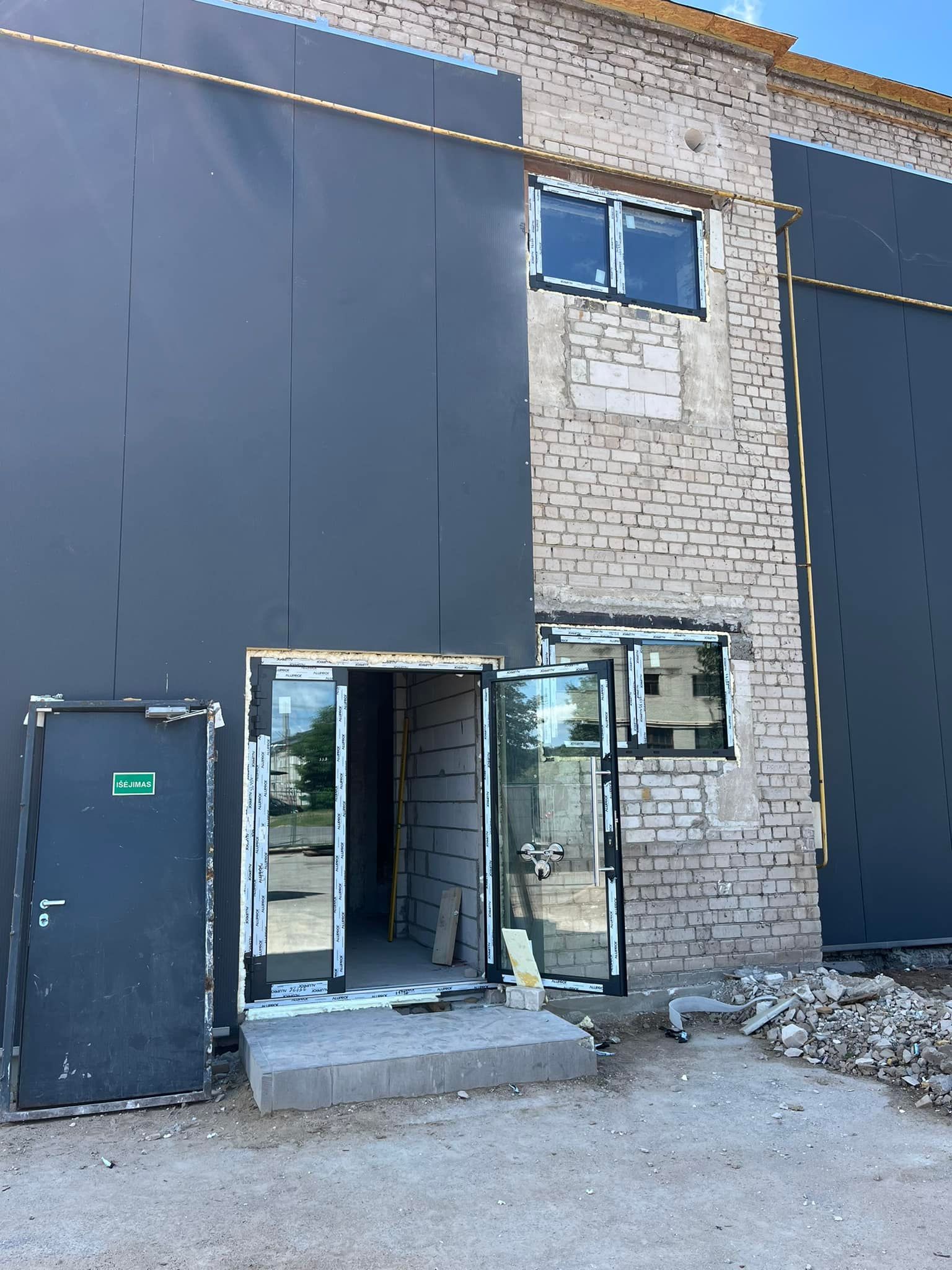 Mūrinis pastatas su juodomis durimis ir žaliu išvažiavimo ženklu