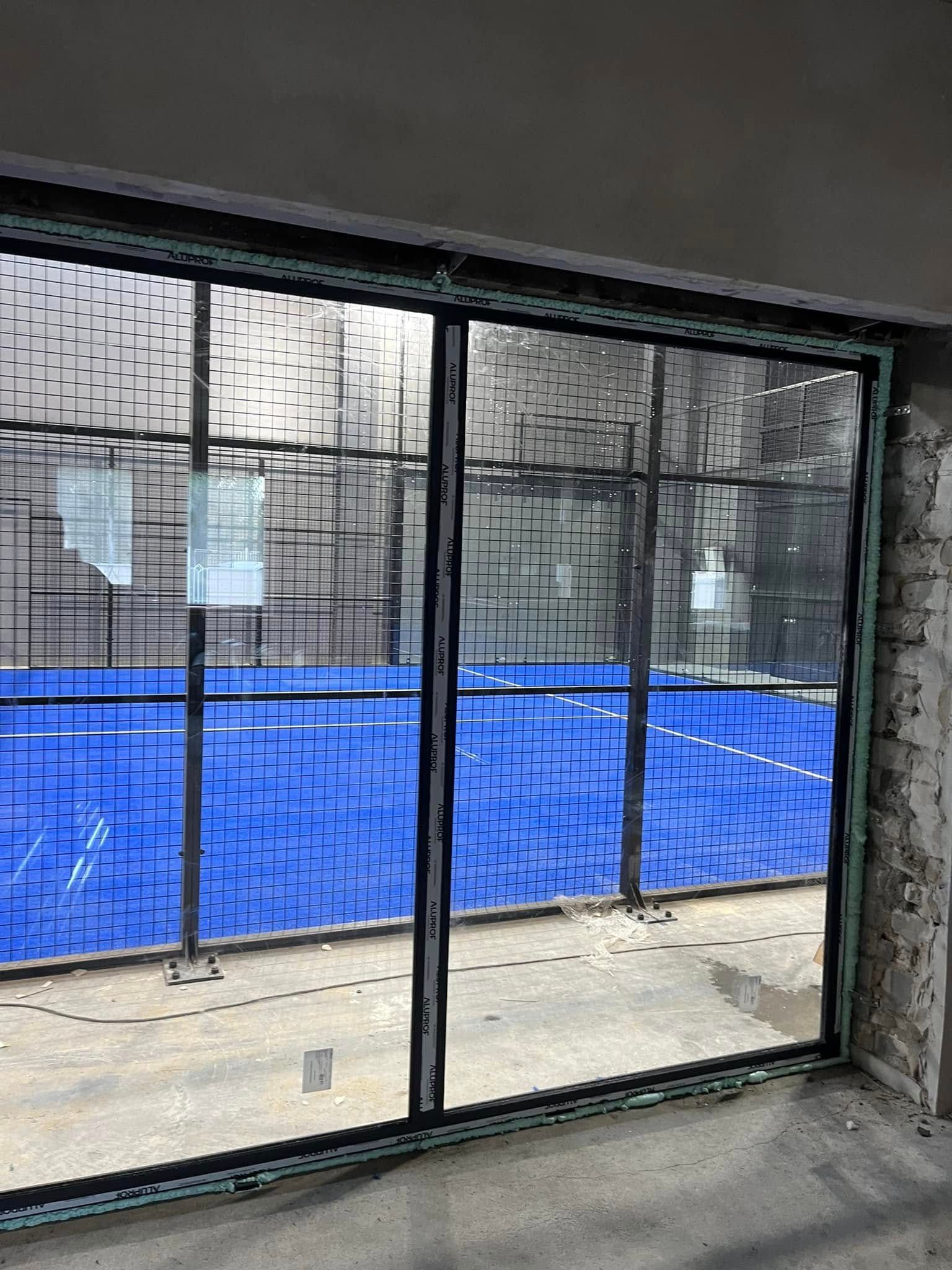 Kambarys su stumdomomis stiklinėmis durimis, vedančiomis į padelio aikštelę.