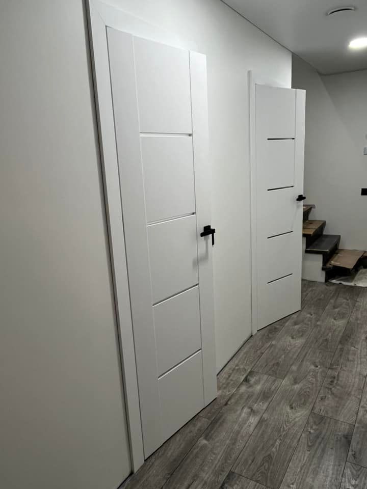 Prieškambaris su baltomis durimis ir laiptais fone.