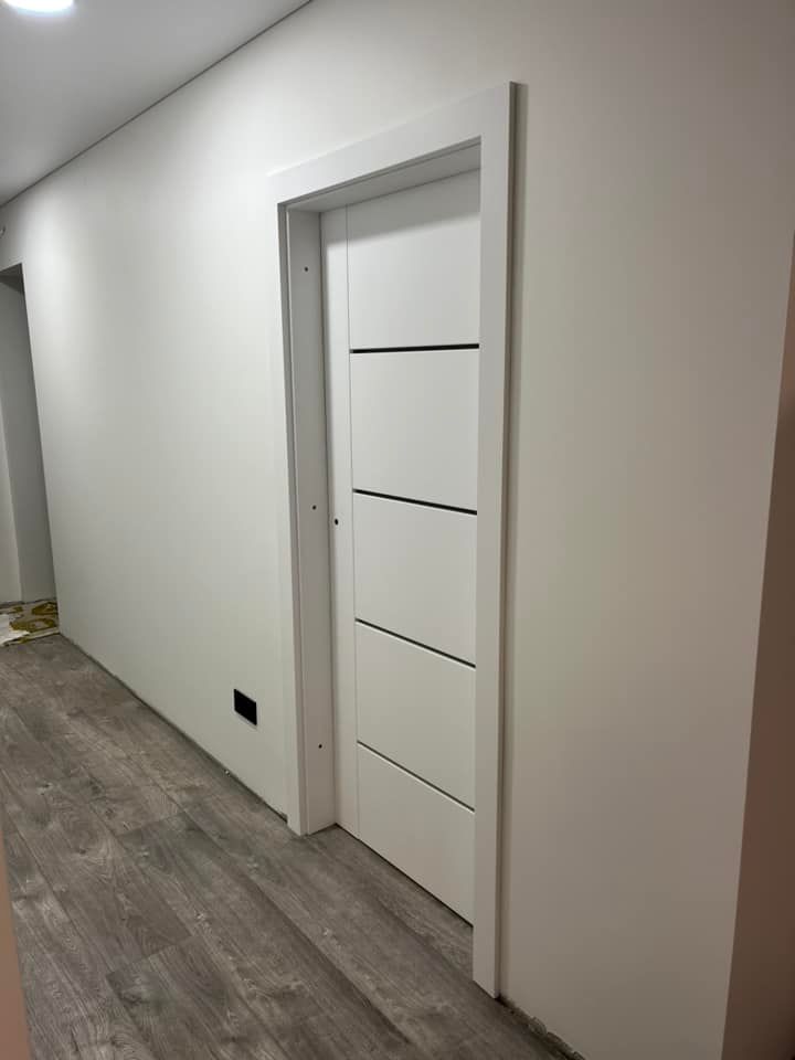 Prieškambaris su baltomis durimis ir medinėmis grindimis.