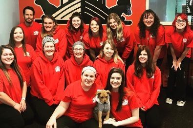 A group of people wearing red shirts are posing for a picture with a dog.
