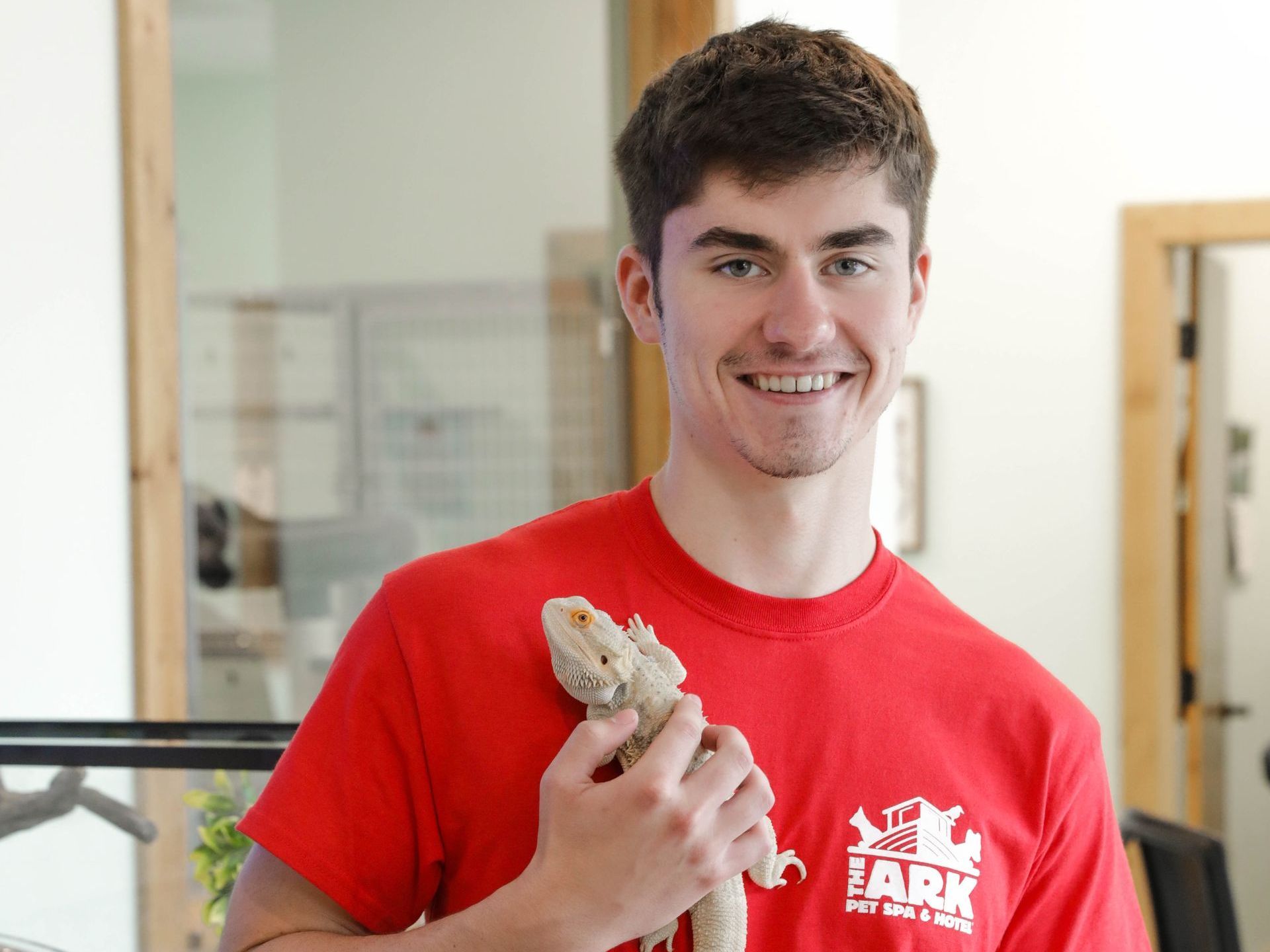 A young man in a red shirt is holding a lizard in his hands.