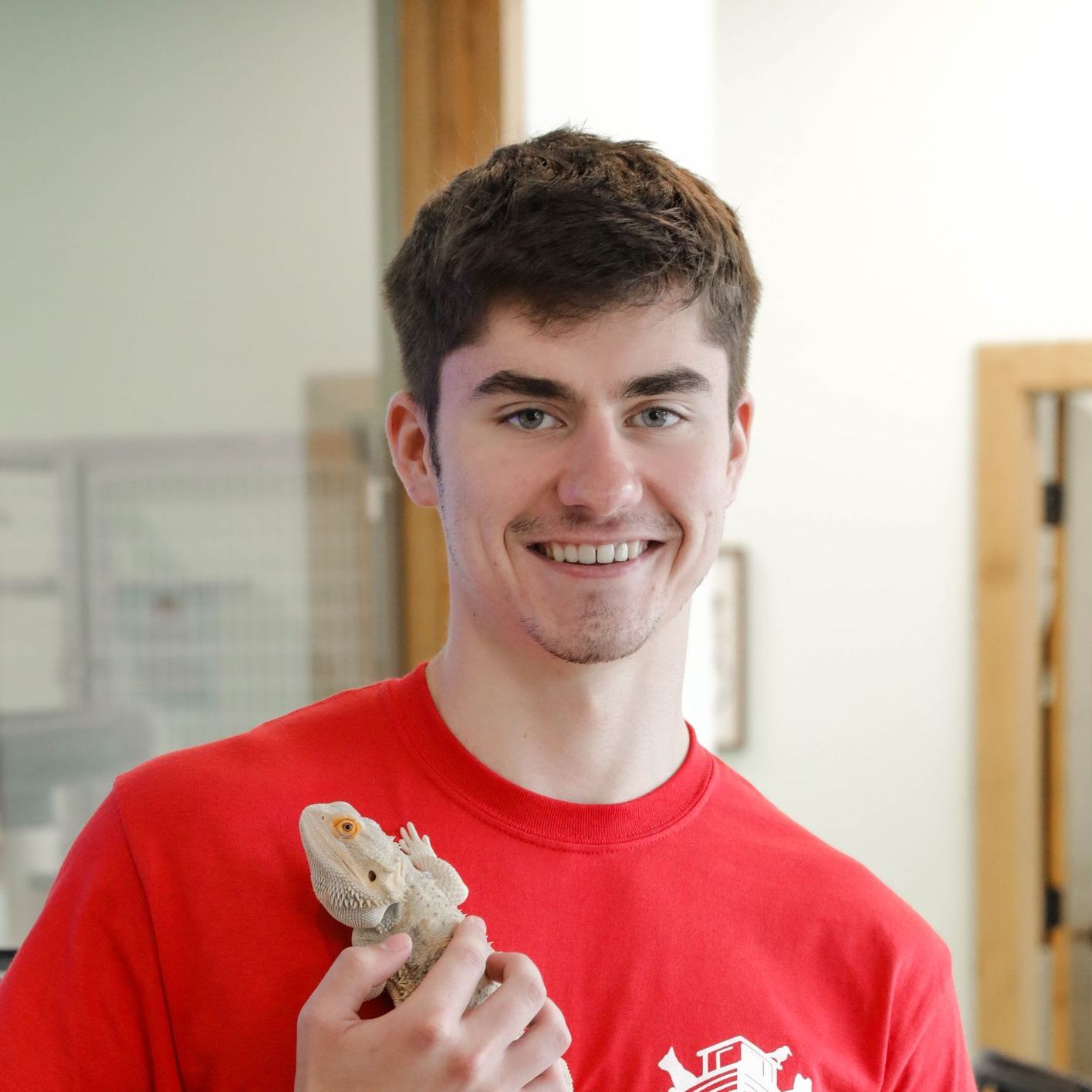 A young man in a red shirt is holding a bearded dragon