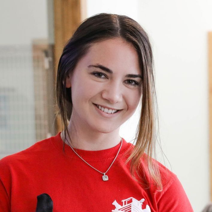 A woman wearing a red shirt and a necklace smiles for the camera.