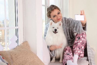 A woman is taking a selfie with her dog while sitting on a window sill.