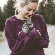 A woman in a purple sweater is holding a kitten in her arms.