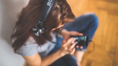 A woman is sitting on the floor wearing headphones and using a cell phone.