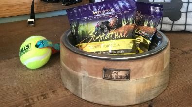 A wooden bowl filled with dog treats and a tennis ball.
