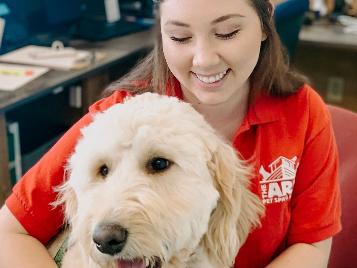 A woman in a red shirt is holding a white dog.