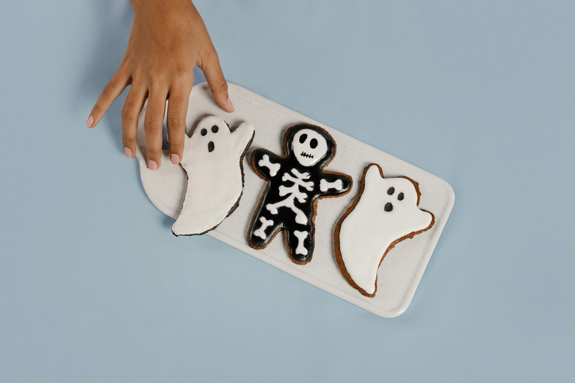 A person is reaching for a tray of halloween cookies.