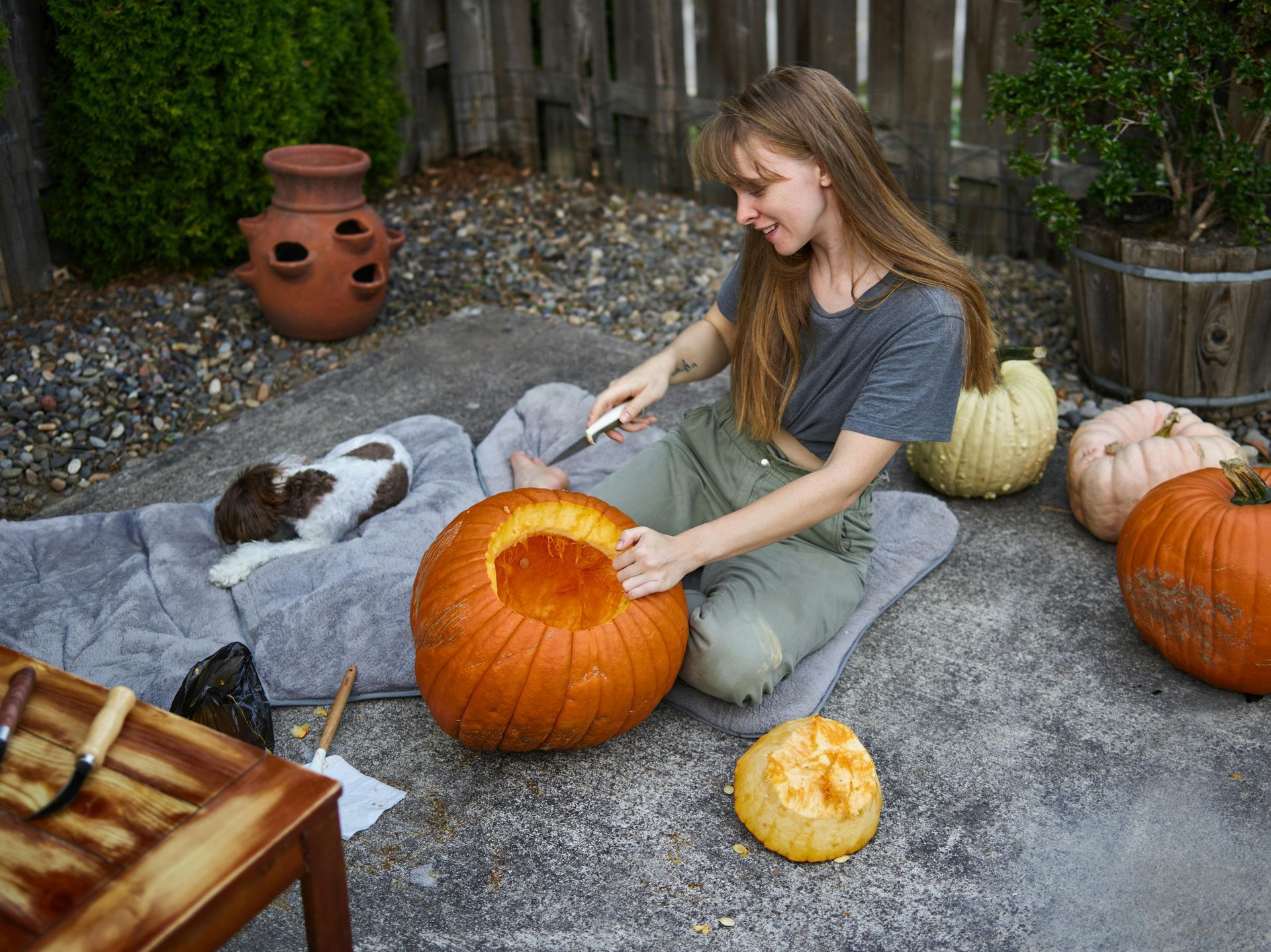 A woman is sitting on the ground carving a pumpkin.
