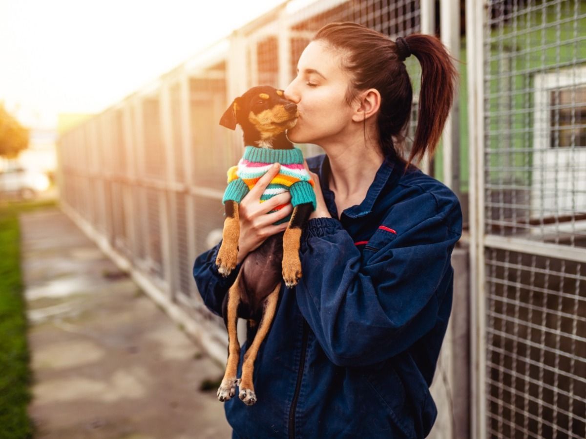 A woman is holding a small dog in her arms and kissing it.