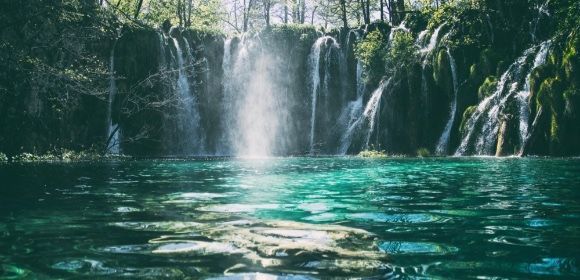 There is a waterfall in the middle of a lake surrounded by trees.