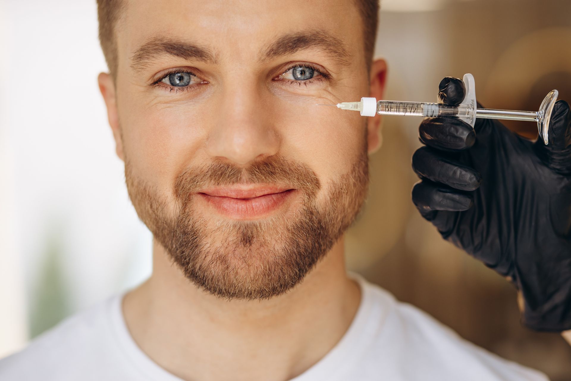 A man with a beard is getting a botox injection under his eye.